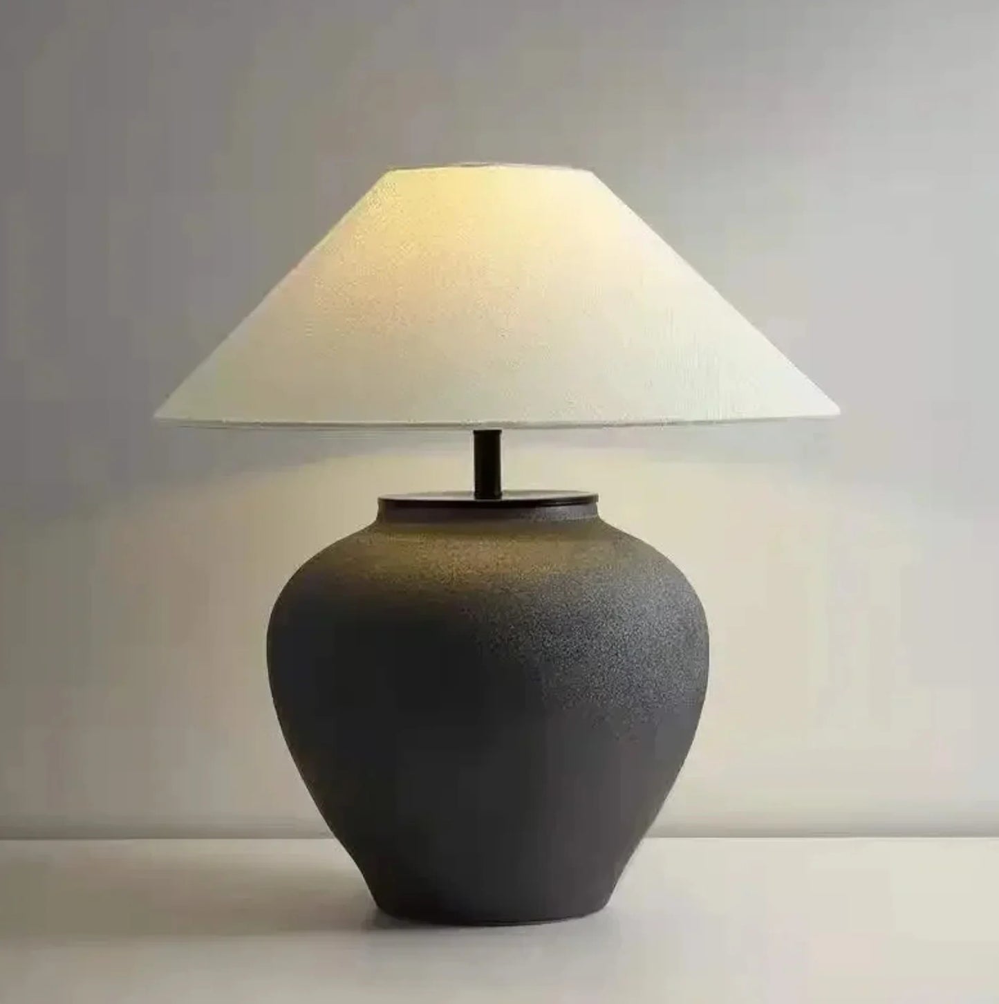 Table lamp with a textured black base and white shade on a neutral background