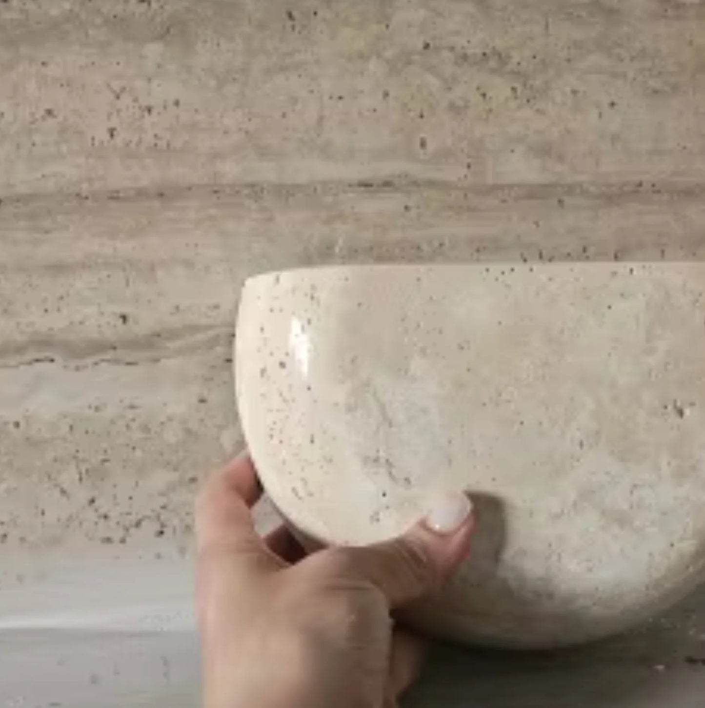 Hand holding a wall light against a beige tiled wall.