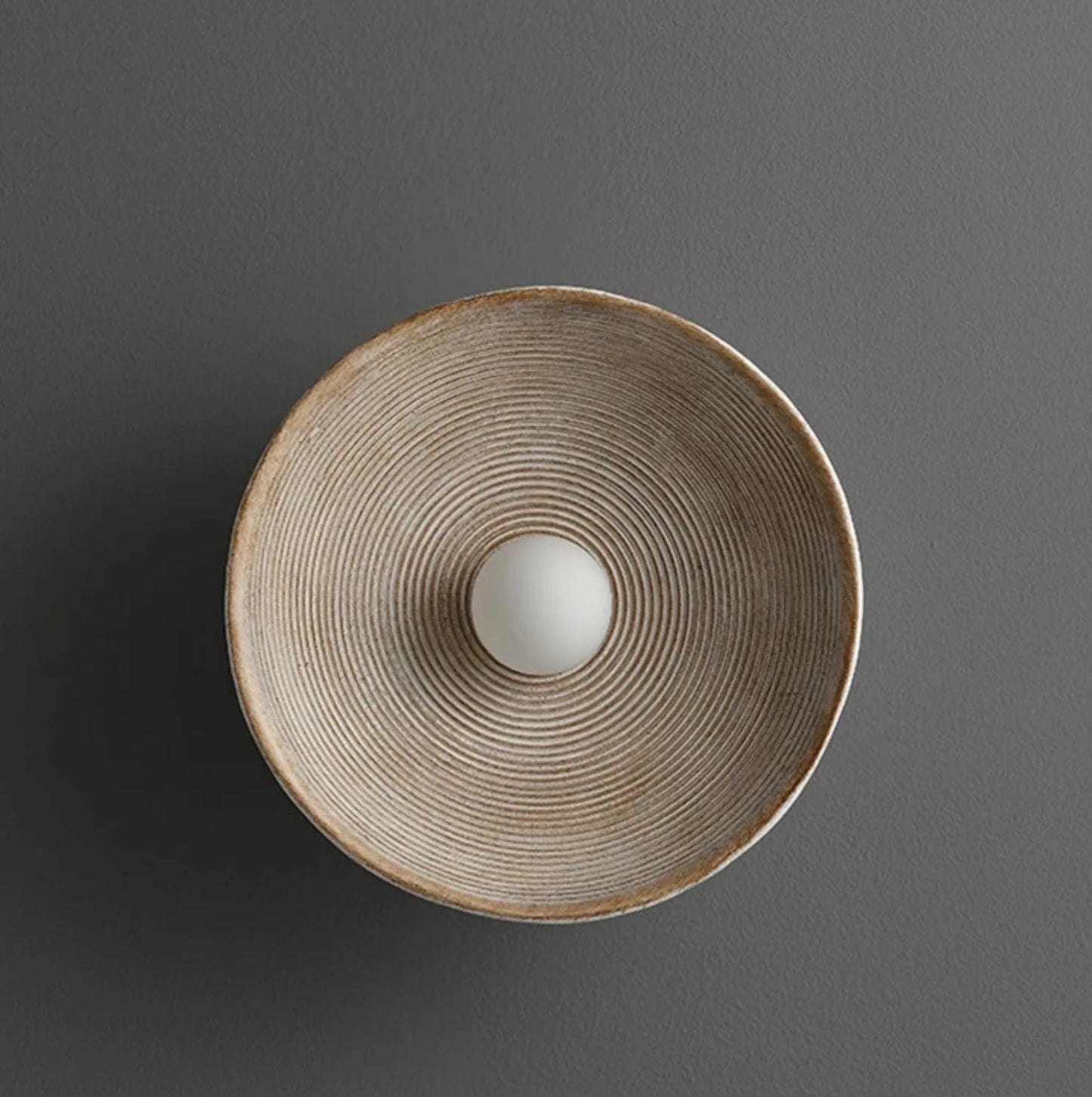 Resine round wall light with textured surface on a gray background