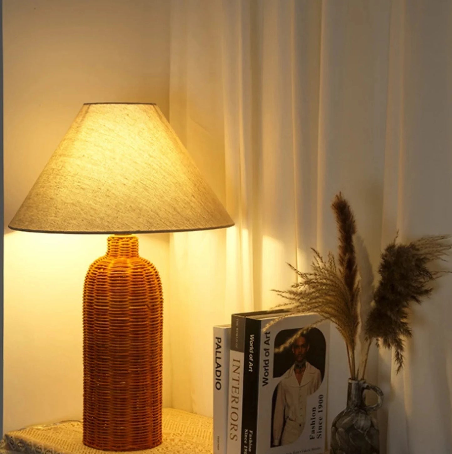 Decorative lamp with a textured base and lampshade, placed on a surface with books and a vase in the background.