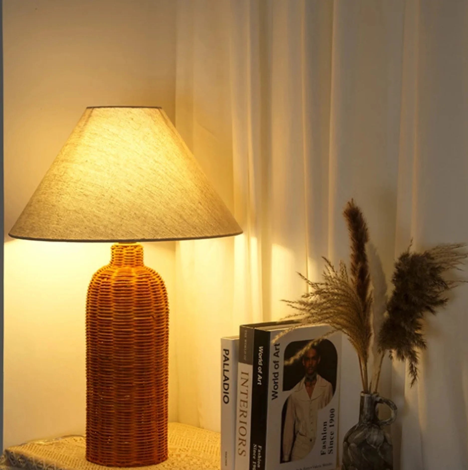 Decorative lamp with a textured base and lampshade, placed on a surface with books and a vase in the background.