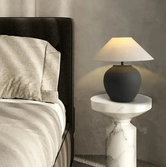 Black table lamp on a marble side table next to a bed with gray bedding.