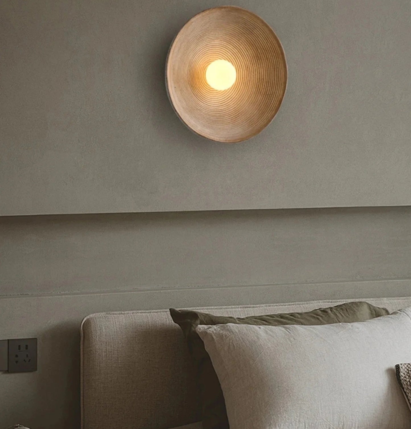 Round wall light fixture on a gray wall above a sofa with pillows.