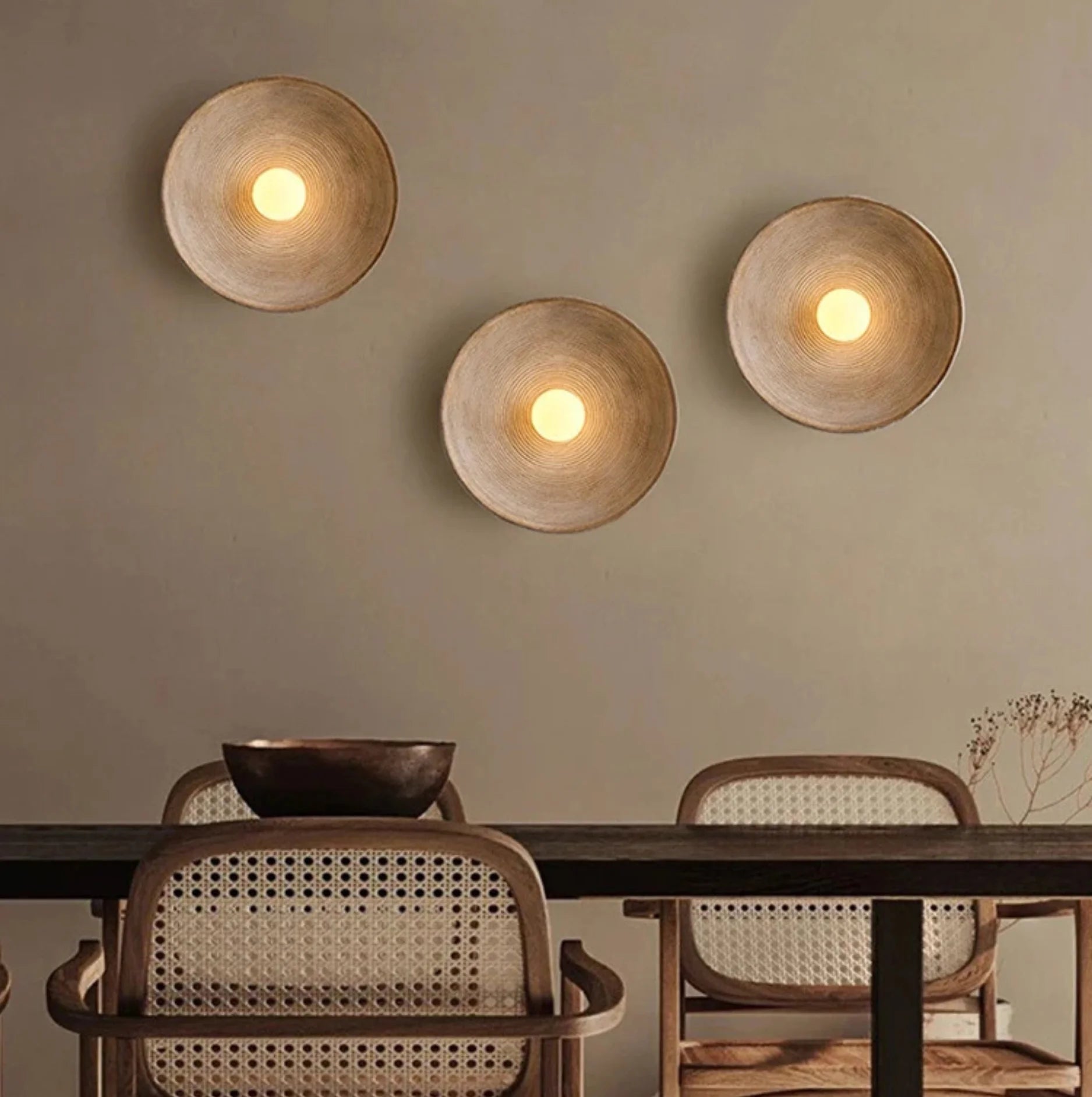 Three wall-mounted round wall lights in a dining room with wooden table and chairs.
