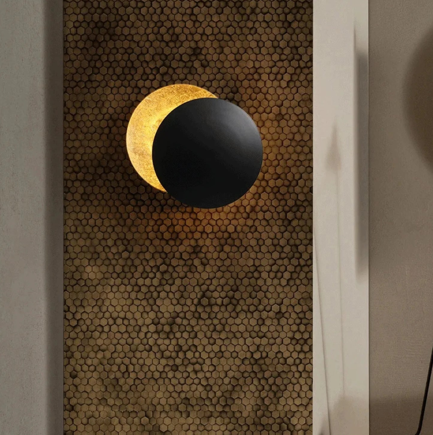 Wall-mounted lamp with black and gold design on a textured wall.