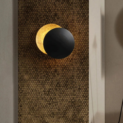 Wall-mounted lamp with black and gold design on a textured wall.