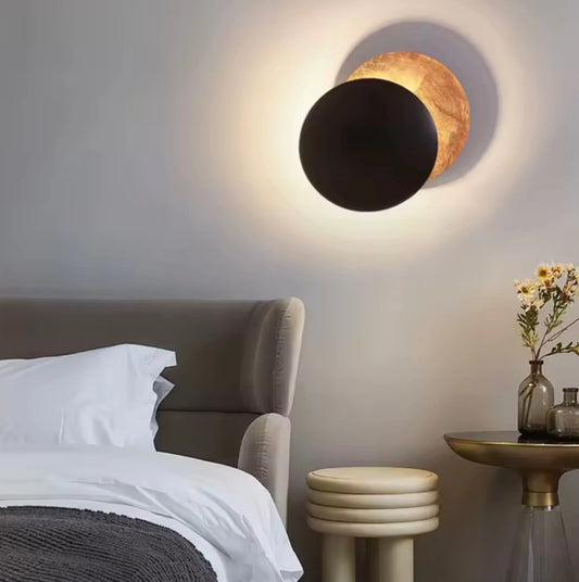 Modern wall lamp with black and gold design in a bedroom setting.