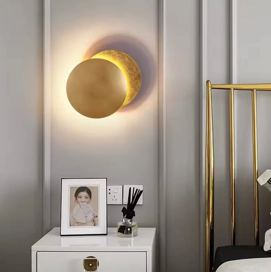 Decorative wall lamp shaped like a moon on a gray wall above a nightstand with a photo frame and diffuser.